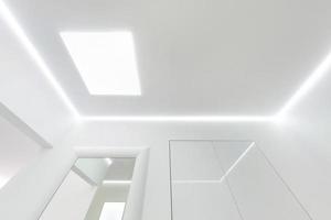 looking up on suspended ceiling with halogen spots lamps and drywall construction in empty room in apartment or house. Stretch ceiling white and complex shape. photo