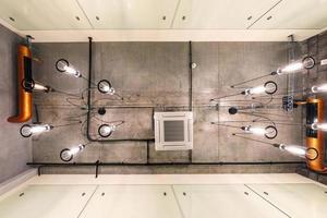 looking up on gray concrete ceiling with halogen spots and edison lamps in loft office room with air conditioning and orange ventilation pipe photo