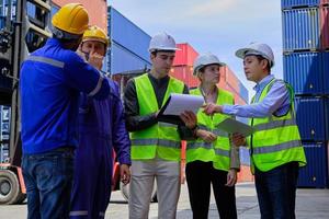 un grupo de trabajadores multirraciales con uniformes de seguridad y cascos trabajan en la terminal logística con muchas pilas de contenedores, control de carga y envío de mercancías para la industria del transporte de carga. foto