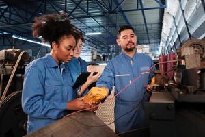 Multiracial professional industry engineer teams in safety uniforms work by inspecting machines' voltage current, checking, and maintaining at manufacture factory, electric system service occupations. photo
