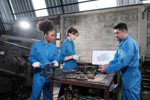 Three multiracial professional industry engineer workers teams in safety uniforms metalwork jobs discuss with mechanical drawing in a monitor, lathe machines, and workshop in manufacturing factory. photo