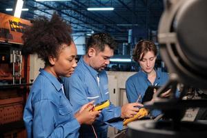 Los equipos multirraciales de ingenieros de la industria profesional con uniformes de seguridad trabajan inspeccionando la corriente de voltaje de las máquinas, comprobando y manteniendo en la fábrica de fabricación, ocupaciones de servicio del sistema eléctrico. foto