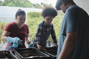 familia de granjeros afroamericanos enseña a su hijo a preparar biofertilizantes juntos con lombrices de tierra en el suelo, aprendizaje de biología y ecología natural, pasatiempo de jardinero orgánico, agricultura rural infantil. foto