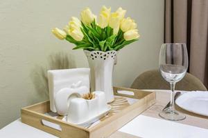 Closeup of empty wine glasses on banquet table with cutlery and Bouquet of yellow tulip flowers photo