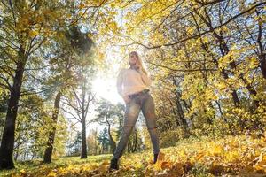 retrato de cerca al aire libre hermosa chica rubia relajarse en el suelo en el bosque de otoño en un día cálido y soleado foto