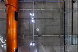 gray concrete ceiling with halogen spots and edison lamps in loft office room with air conditioning and orange ventilation pipe. looking up photo