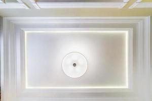 looking up on suspended ceiling with halogen spots lamps and drywall construction in empty room in apartment or house. Stretch ceiling white and complex shape. photo