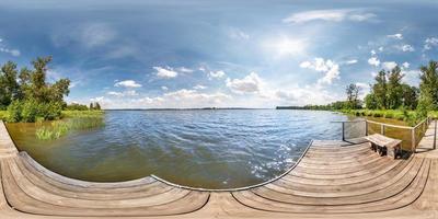 panorama hdri esférico completo sin costuras vista en ángulo de 360 grados en el muelle de madera de un enorme lago o río en un día soleado de verano y clima ventoso con hermosas nubes en proyección equirectangular, contenido vr foto