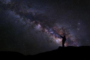 A Man is standing next to the milky way galaxy pointing on a bright star, Long exposure photograph, with grain photo