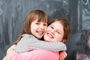 little girls hugging in front of chalkboard photo