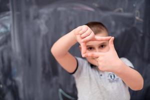 happy boy making hand frame gesture in front of chalkboard photo