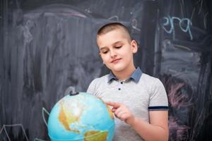 boy using globe of earth in front of chalkboard photo