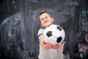 niño feliz sosteniendo una pelota de fútbol frente a la pizarra foto