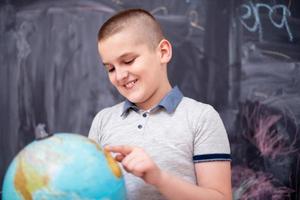 boy using globe of earth in front of chalkboard photo