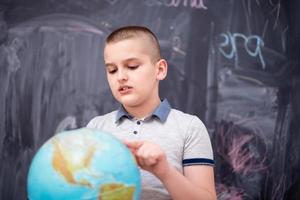 boy using globe of earth in front of chalkboard photo