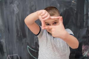 happy boy making hand frame gesture in front of chalkboard photo