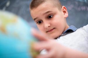 boy using globe of earth in front of chalkboard photo