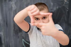 happy boy making hand frame gesture in front of chalkboard photo