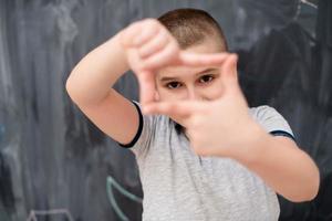 happy boy making hand frame gesture in front of chalkboard photo