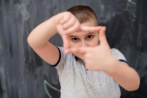 happy boy making hand frame gesture in front of chalkboard photo