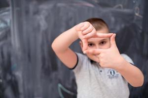 happy boy making hand frame gesture in front of chalkboard photo