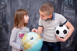 boy and little girl using globe of earth in front of chalkboard photo