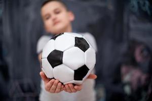 niño feliz sosteniendo una pelota de fútbol frente a la pizarra foto