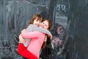 little girls hugging in front of chalkboard photo