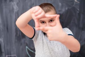 happy boy making hand frame gesture in front of chalkboard photo