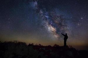 un hombre está de pie junto a la galaxia de la vía láctea apuntando a una estrella brillante, fotografía de larga exposición, con grano