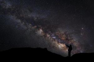 un hombre está de pie junto a la galaxia de la vía láctea apuntando a una estrella brillante, fotografía de larga exposición, con grano