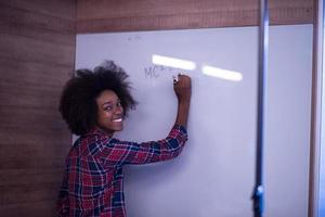 African American woman writing on a chalkboard in a modern office