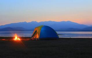 carpa y fogata al atardecer, al lado del lago foto