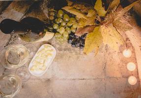 Top view of cheese, white wine glasses, grapes and autumn leafs with bottle of wine. Flat lay of wine set up and background image. photo