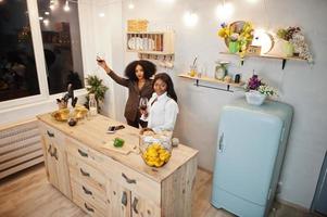 Two african american female friends women spending time at kitchen with wine. Black girlfriends  relaxing at home. photo