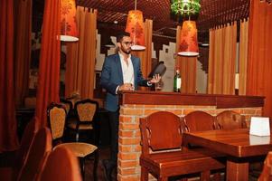 Handsome well-dressed arabian man with glass of whiskey and cigar posed at pub. photo