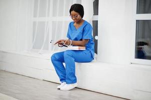 Portrait of happy female african american young doctor pediatrician in blue uniform coat and stethoscope with books at hands. Healthcare, medical, medicine specialist - concept. photo