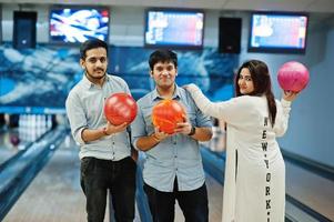 tres amigos del sur de asia con camisa de jeans en el club de bolos sosteniendo pelotas en las manos. foto