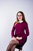 retrato de una mujer joven con vestido morado y gafas sentada en la silla del estudio. foto