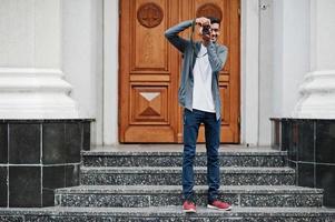 Stylish indian young man photographer wear casual posed outdoor with dslr photo camera at hands.