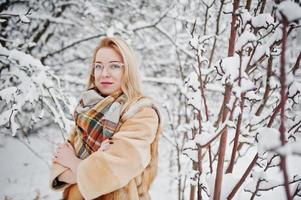 Portraiy of blonde girl in glasses, red fur coat and scarf at winter day. photo