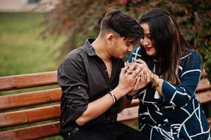 Love story of indian couple posed outdoor, sitting on bench together. photo