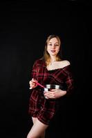 Young housewife in checkered dress with saucepan and kitchen spoon isolated on black background. photo