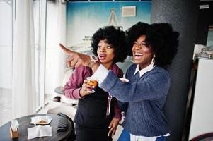Two curly hair african american woman wear on sweaters with cups of tea posed at cafe indoor. photo