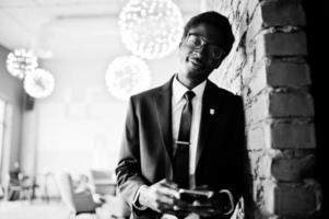 Business african american man wear on black suit and glasses at office looking on mobile phone. photo