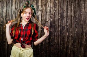 joven ama de casa divertida en camisa a cuadros y pantalones cortos amarillos pin up estilo sobre fondo de madera. foto