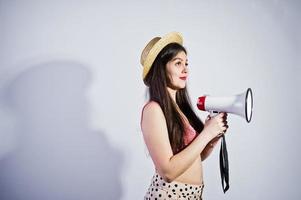 Portrait of a gorgeous young girl in swimming suit and hat talks into megaphone in studio. photo