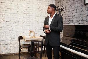 Strong powerful african american man in black suit standing against piano. photo