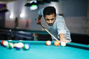 Stylish arabian man wear on jeans playing pool billiard on bar. photo