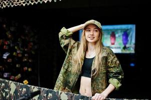 Military girl in camouflage uniform against army background on shooting range. photo